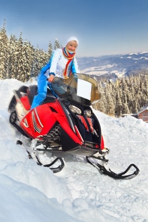 Smiling young woman riding a snowmobile against winter landscape